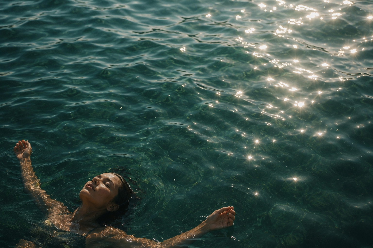 Floating on the surface of calm, sunlit sea water, face turned to the sky