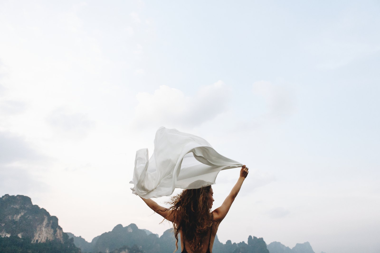 A woman releasing a white cloth into the wind against an open sky